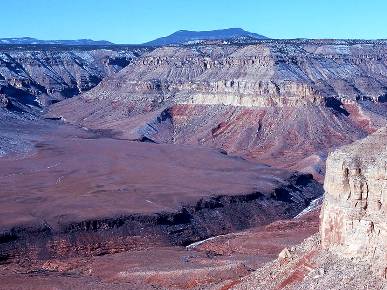 multiple rock layers are visible in a canyon cut by a river below