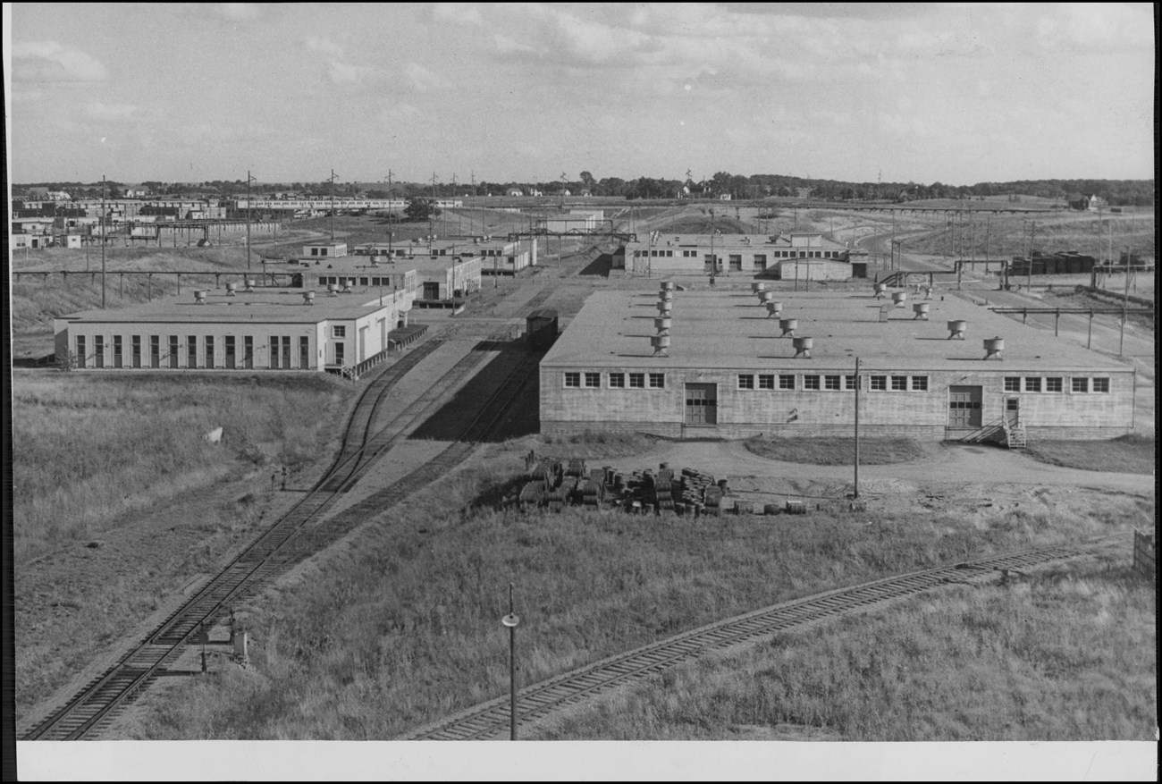 Aerial photograph looking into the distance at several rows of identical concrete industrial, warehouse-like buildings with rail lines and roads winding through the spaces between them