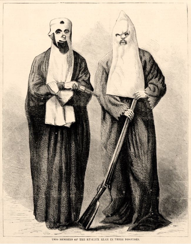 Two white men wearing robes and white hoods covering their faces while holding guns.