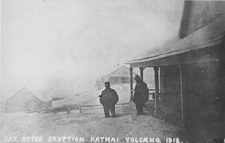 Historic photo of two men standing outside of ash covered buildings