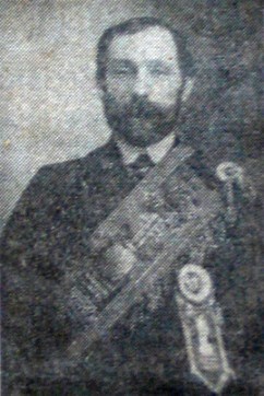 Black and white photo of man with dark hair and beard in suit and regalia.