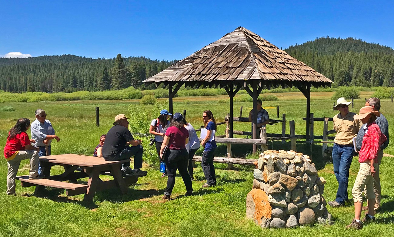 Tásmam Kojóm Maidu Park A group gathers at an interpretive site with a wooden gazebo at a sunny and grassy Yellow Creek Campground.