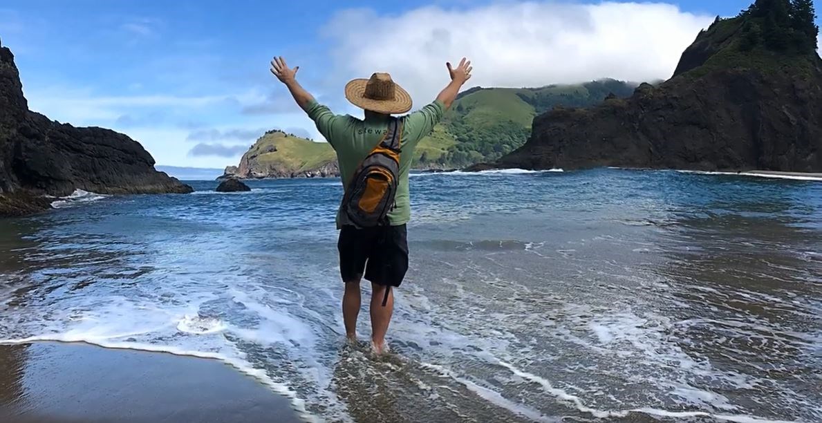 man stands in ocean near rocks with his hands in the air