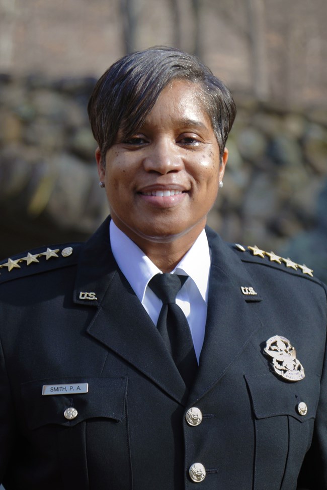 Pamela A. Smith, Chief of United State Park Police stands in front of a stone bridge in Rock Creek Park.