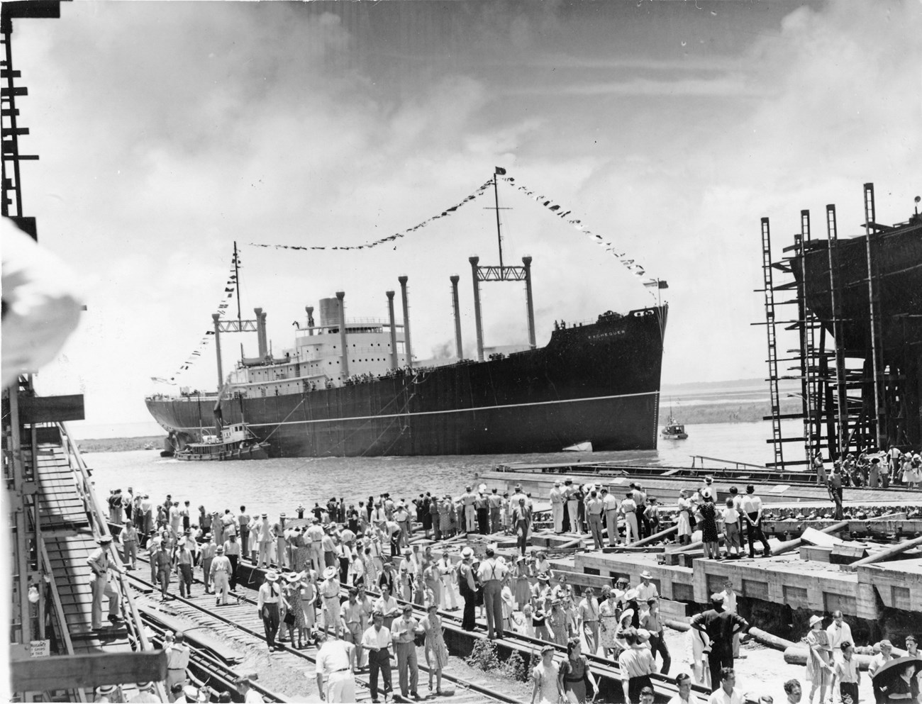 SS Exchequer, American Export Lines. AP News. Black and white photo of a crowd gathered on a pier with a large ship festooned with flags just off the dock. Scaffolding on either side