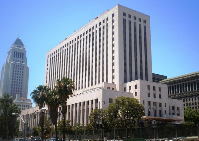 Color photo of 17-story Art Moderne-style building with pale walls. It is rectangular and steps back at the 4th & 6th stories with a slab-like tower rising above. The windows are organized in vertical strips and set back from the facade.
