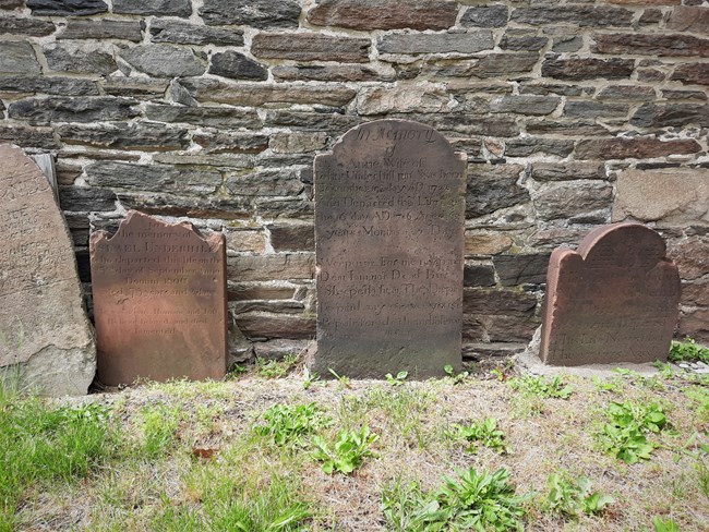 small, reddish brown gravestones, set against a stone wall