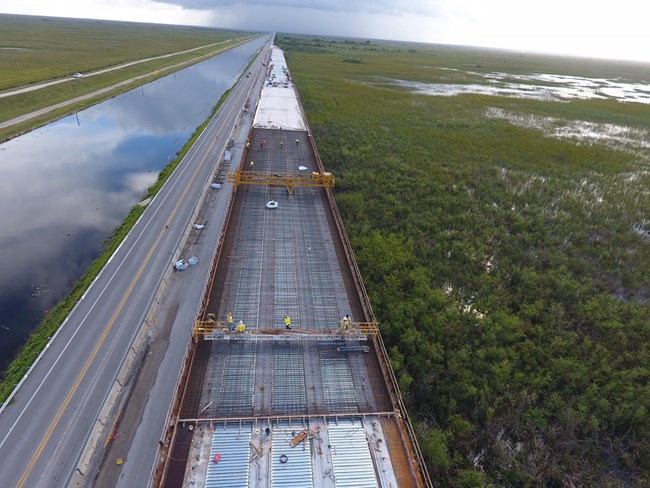 Construction is shown on an elevated bridge above the Everglades.