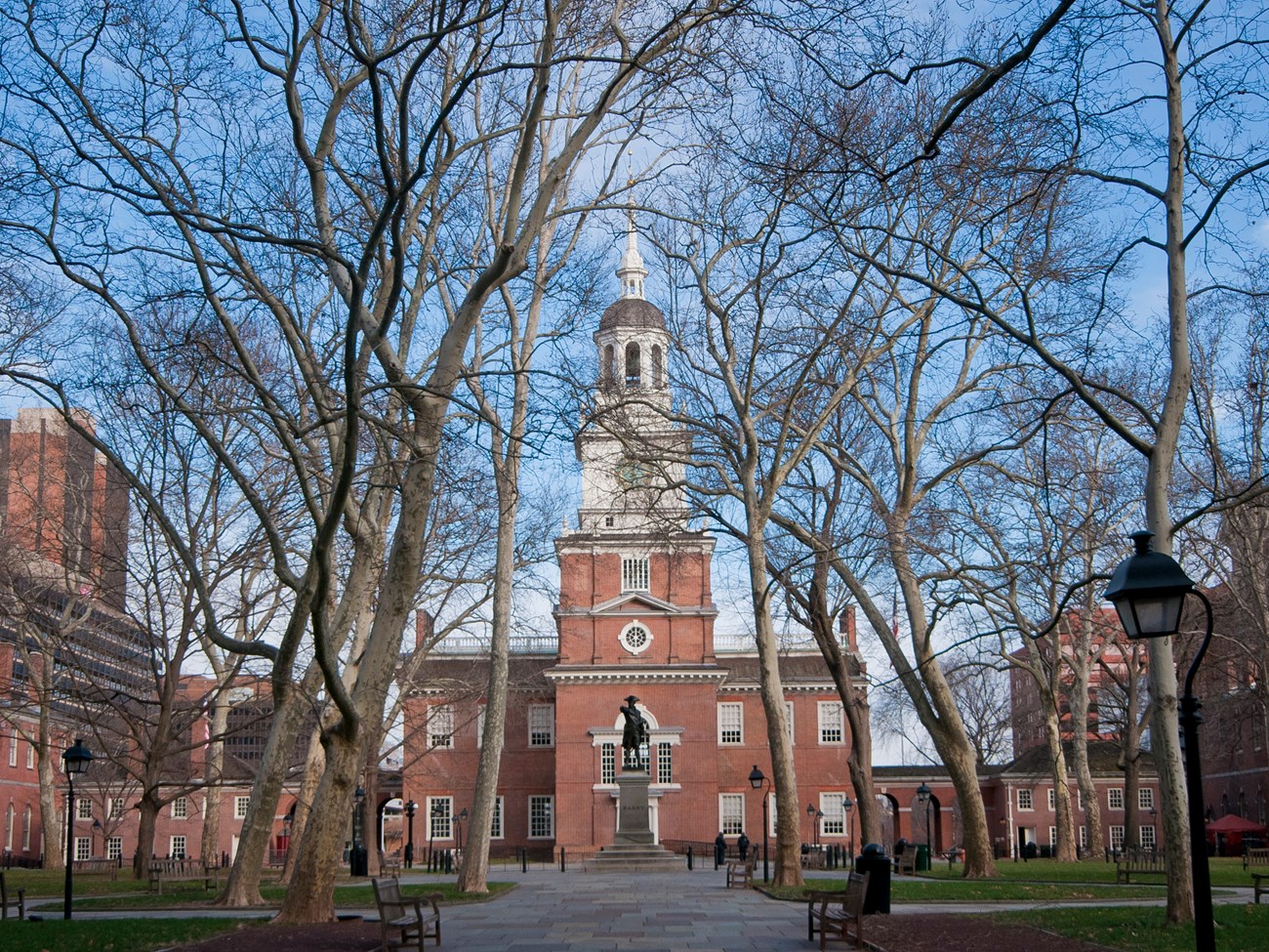 Independence Square Two story brick building with white clock tower and cupola and a statue of a man in a tricorner hat standing on a pedestal