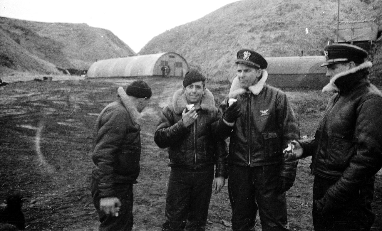 Four men in cold weather gear in front of rounded buildings.