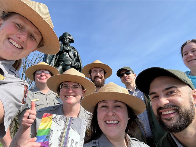 A group of smiling rangers in front of a bronze statue of a soldier.