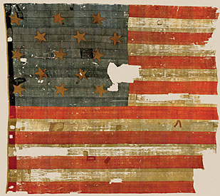 An American flag with 15 stripes and 15 stars. It is visibly tattered and displays some holes.