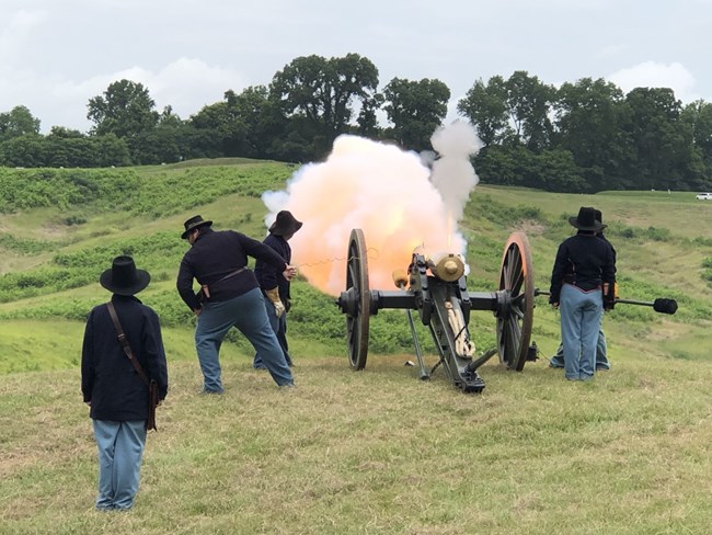 A group of volunteers dressed in Civil War clothing stand near a cannon that has been fired