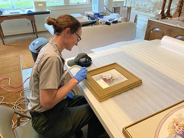 A National Park Service employee carefully cleans a framed painting.