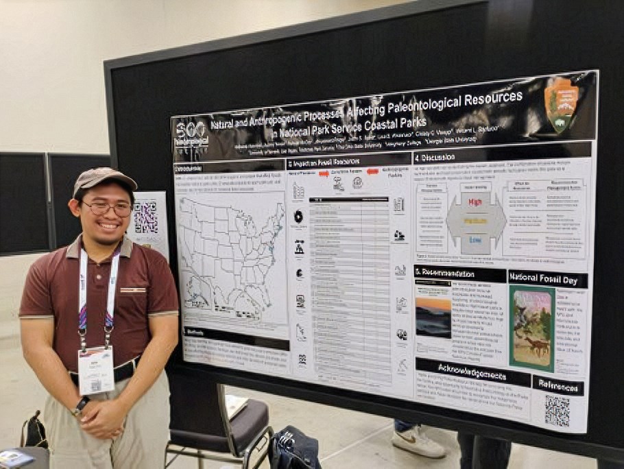 A smiling person standing next to a poster mounted on a broad vertical display surface.