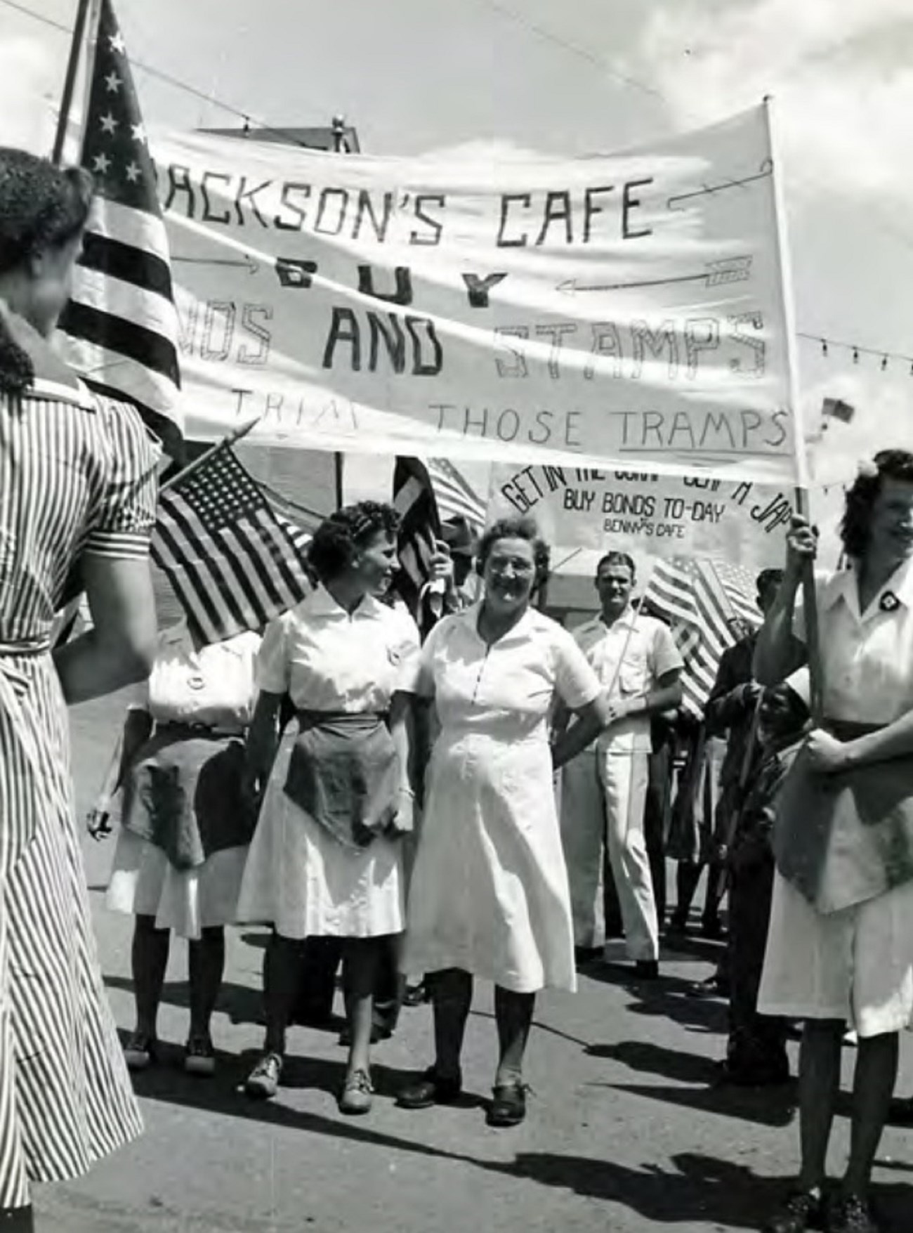 Men and women carrying banners while walking in a War Bond Drive parade