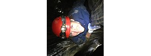 Michelle in a red hard hat, headlamp, and gloves, viewed from above as she climbs a tree at night.