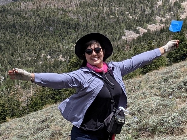 Vianey_Murphy Woman with her arms spread wide and smiling, holding a plot marker at a sagebrush monitoring site.