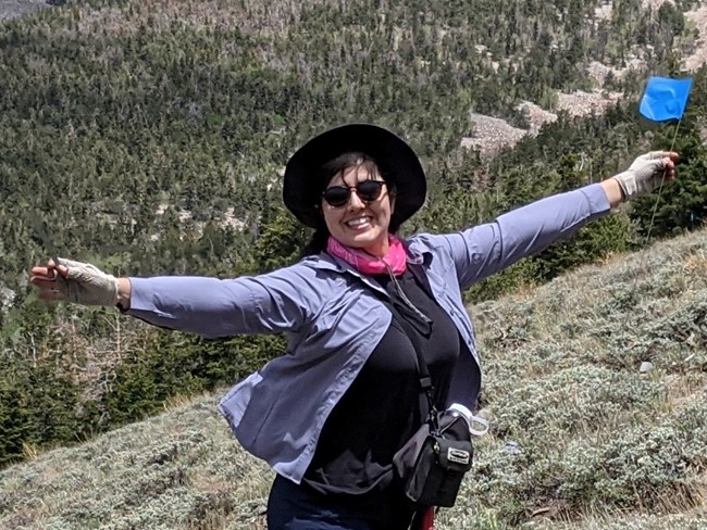 Woman with her arms spread wide and smiling, holding a plot marker at a sagebrush monitoring site.