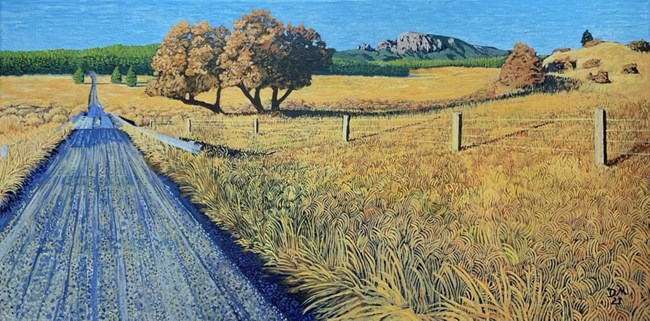 A road crosses a field of golden grass punctuated by trees, rocks, and a fence