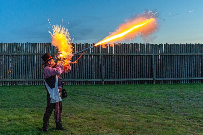 Sparks fly from a musket fired by a reenactor in period costume