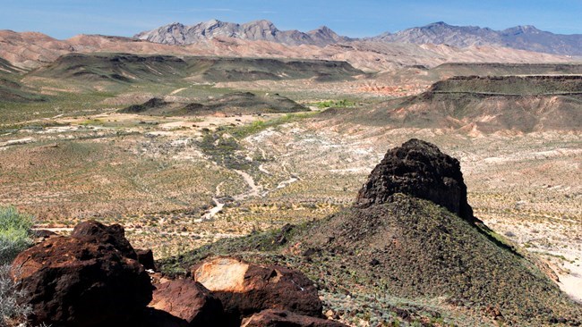 photo of a dark rock outcrop (volcanic neck) with desert landscape in the distance