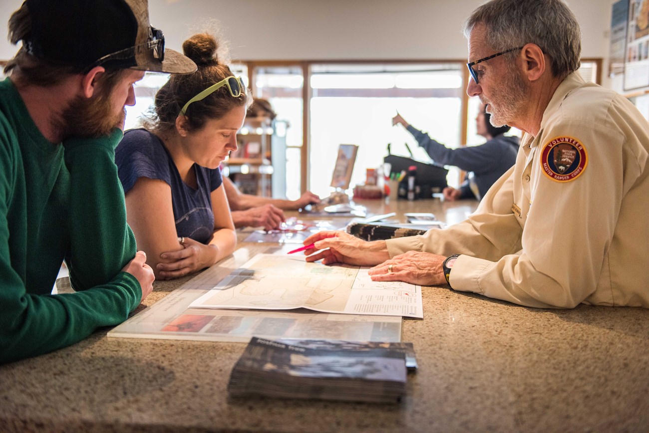 a man in a volunteer uniform gives trip planning advice to two visitors