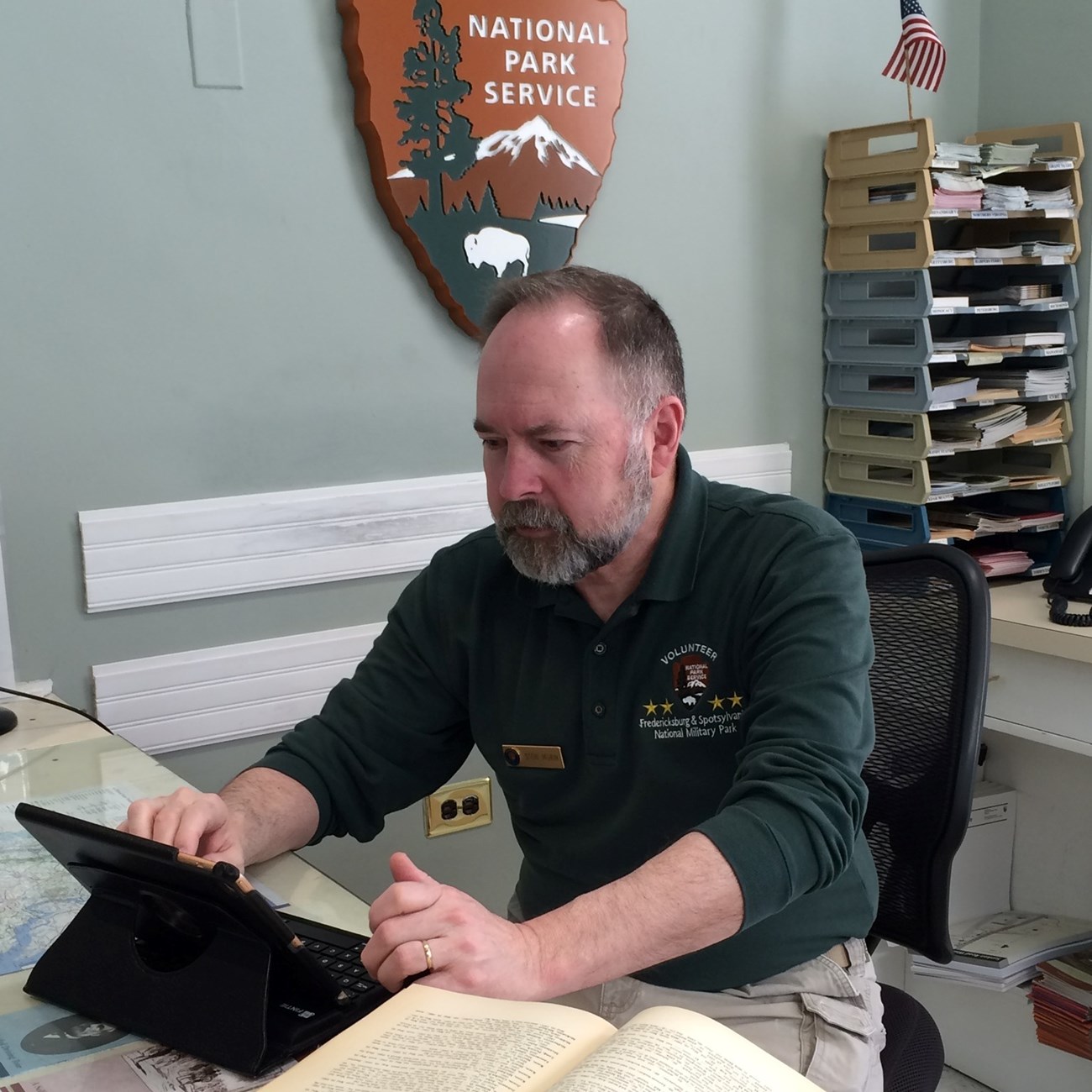Volunteer Spotlight Steve Fredericksburg and Spotsylvania National Military Park volunteer Steve Morin, seated at the Fredericksburg Battlefield Visitor Center front desk. He is doing research work with a laptop and open book on the desk in front of him.