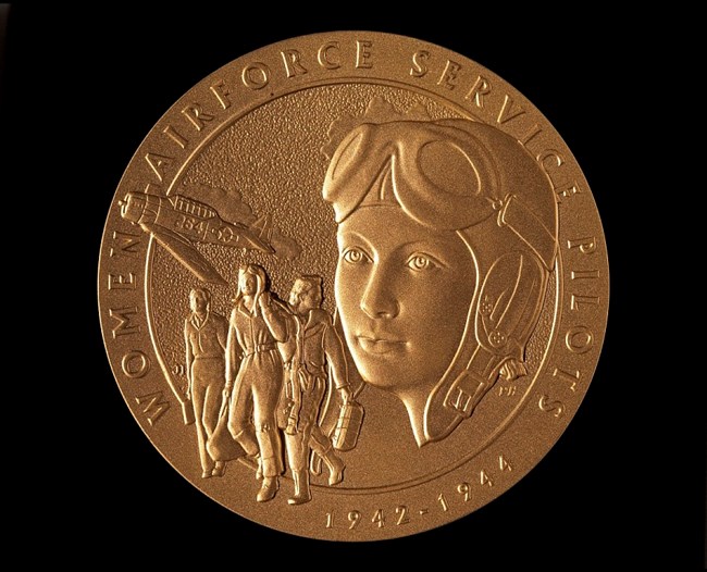 Close-up image of a cast medal with images of women pilots and the text Women's Airforce Service Pilots around the edge