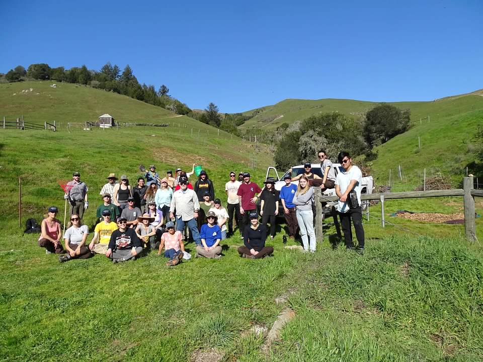 Volunteers near planting site 34 people gathered outside on a grassy landscape.