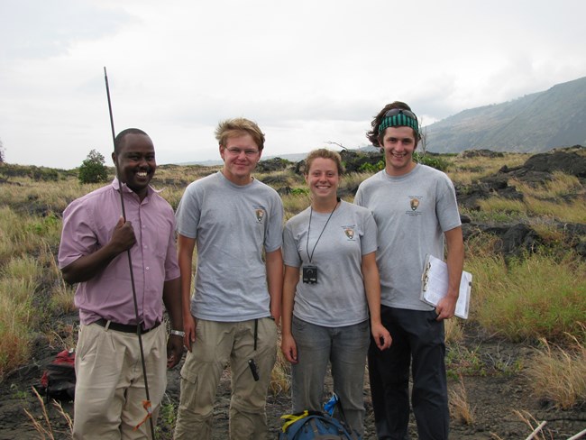 four young people posing for picture with mountain in the background