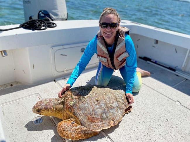 woman stands on boat next to large sea turtle