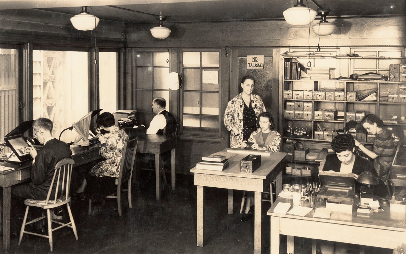 Men and women working over magnifying viewers to paint lantern slides.