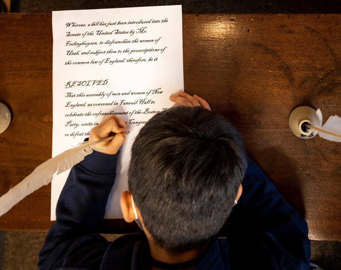 A child signing a document with a quill pen