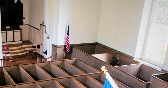 Church interior, with high walled wooden pews, flags visible