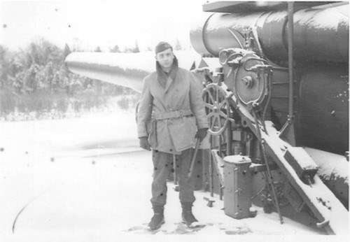 a young soldier in a coat stands in front of a snowy gun battery