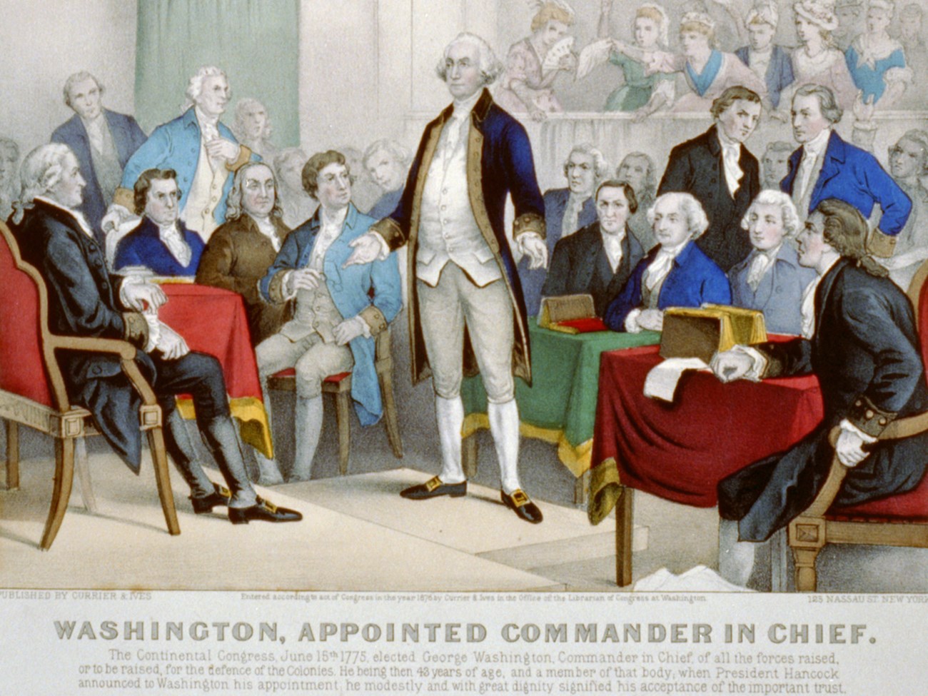 George Washington's Commission as Commander in Chief White man in a long blue coat standing in the center of a room with a crowd of people looking at him.