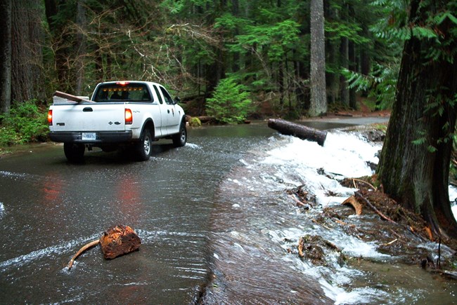 A white truck sits atop a paved road covered in a small flood of water