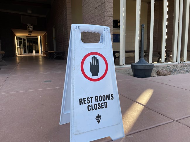 White temporary sign, "Restrooms closed" in front of cinder block building.