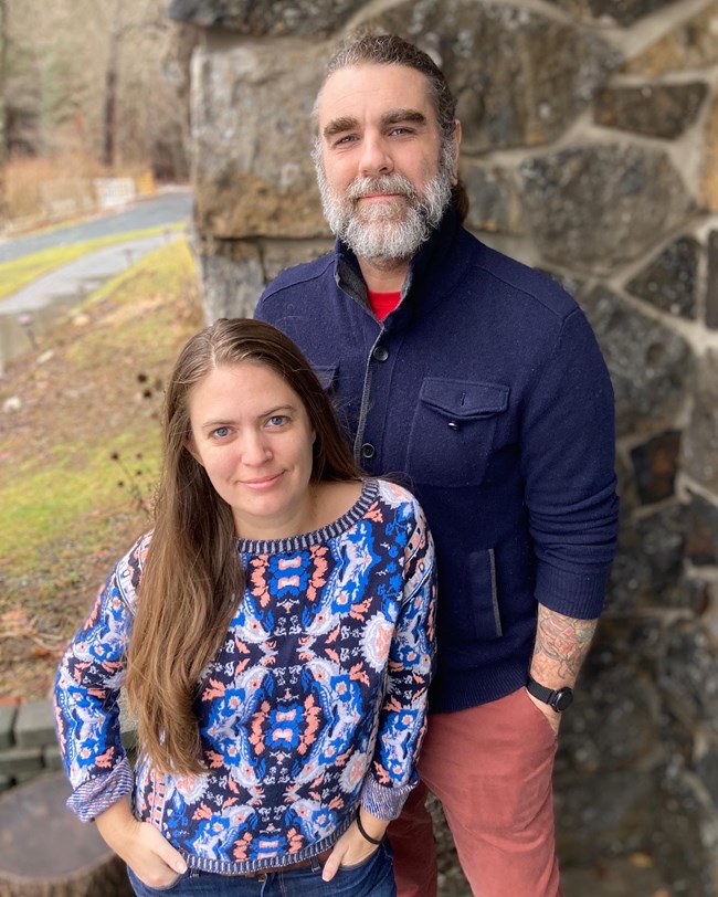 Woman and man stand in front of a stone wall