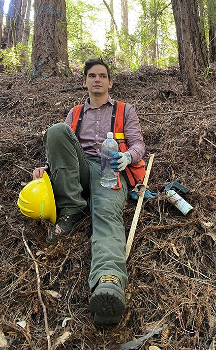 man sits on forest floor with scientific equipment around him