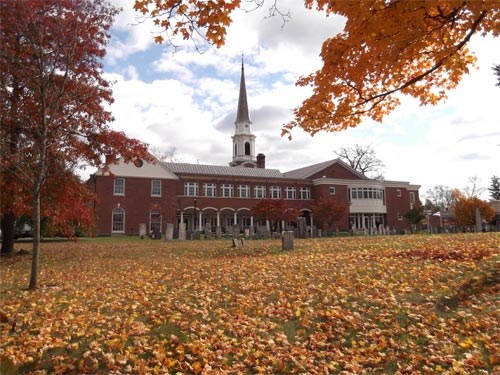color photo of the exterior of a brick church surrounded by fall colors
