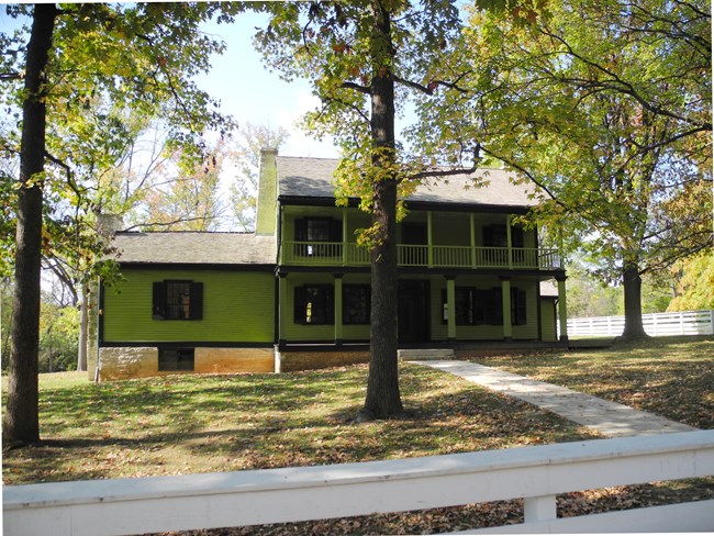 Green house behind a green lawn and trees in front
