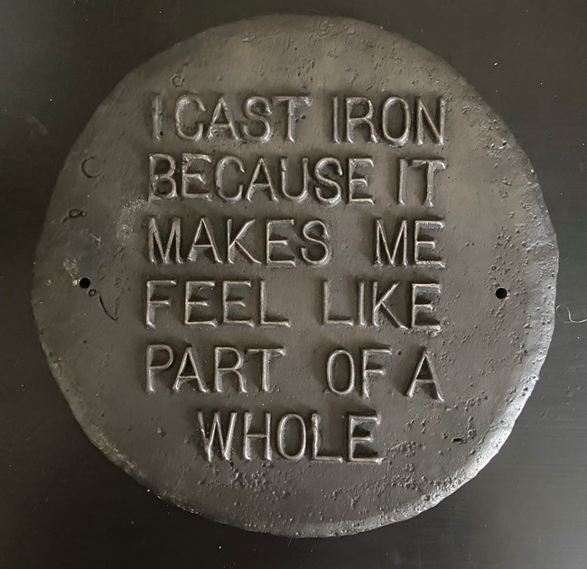 Circular cast iron plaque with "I cast iron because it makes me feel like part of a whole" on it