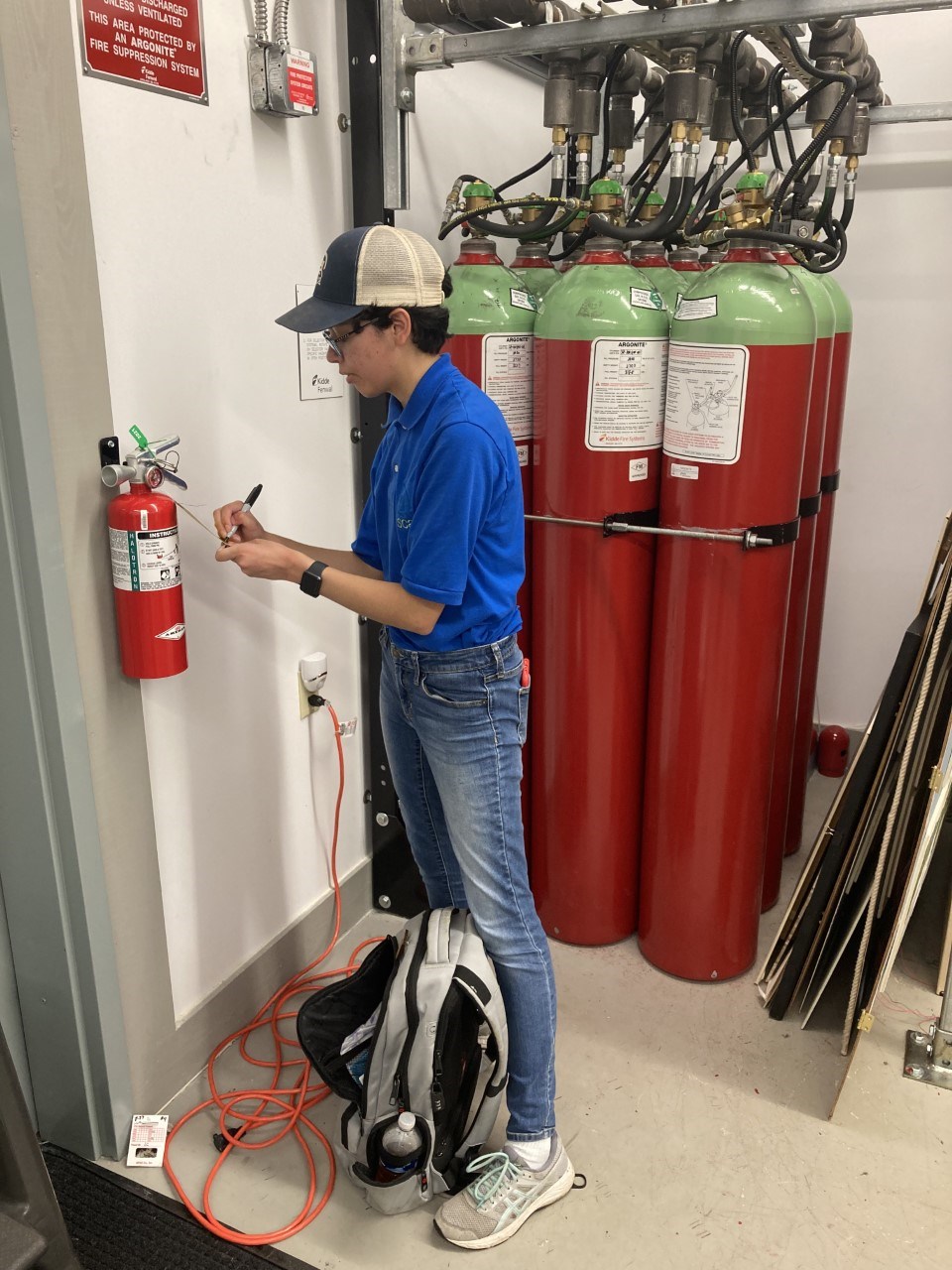 Structural Fire Protection Intern Lisa Weir Person writes on a clipboard while looking at a fire extinguisher.