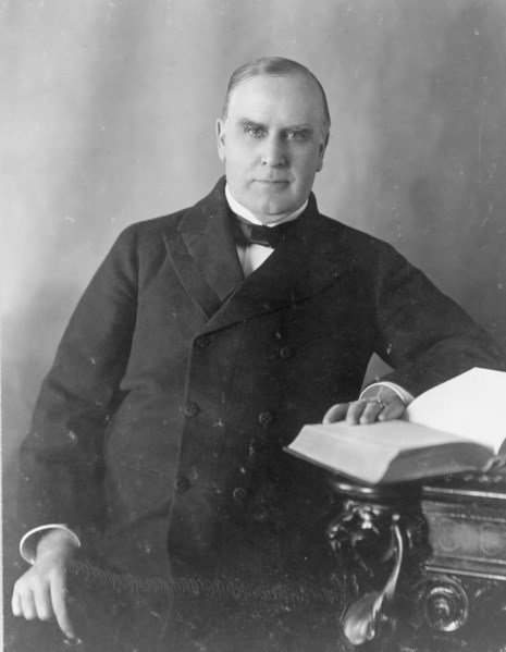 President McKinley sitting at a table with a book open.