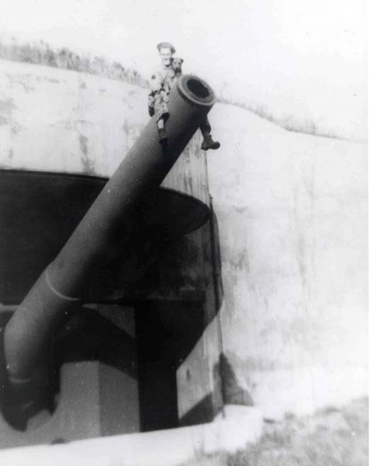 a young man sits on a battery gun holding a small dog