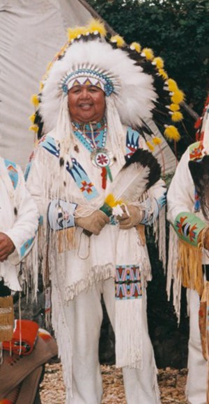 Tribal elder man, headdress of black & white feathers, white buckskin pants, shirt with beadwork.