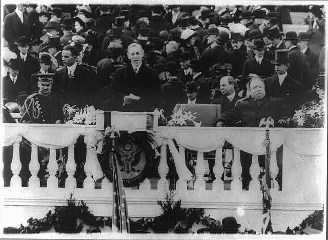 President Wilson standing at a podium before a crowd giving an inaugural address in 1913 President Wilson standing at a podium before a crowd giving an address in 1913