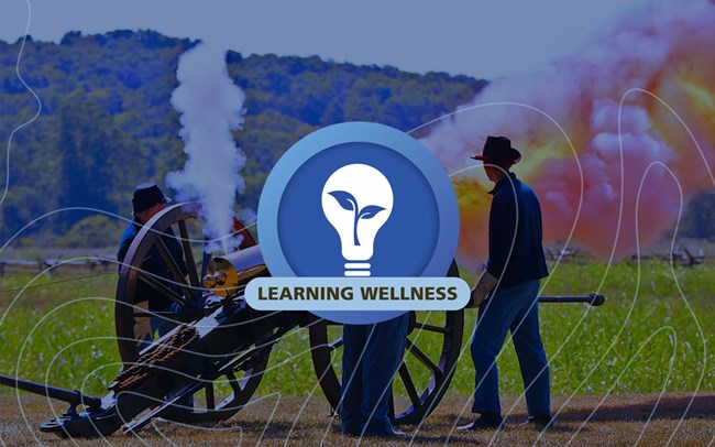 A circular blue graphic with a lightbulb containing a plant in the center and the words learning wellness, graphic is on top of blue tinted photo of the  Bloody Hill tour stop hiking trail at the sinkhole surrounded by split rail fencing for protection.
